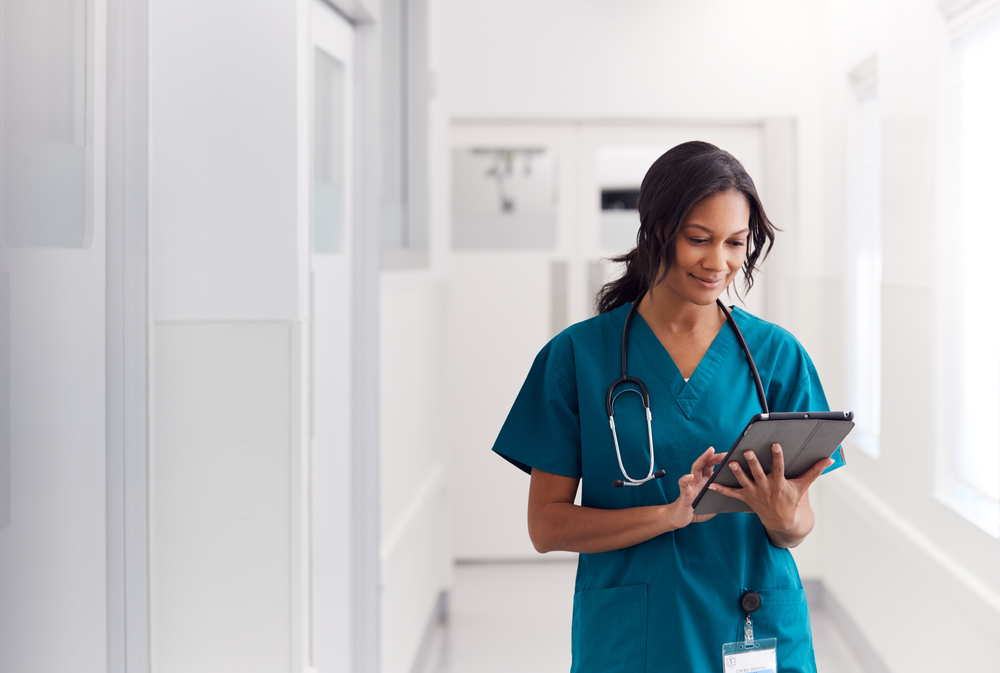 Female nurse Wearing Scrubs In Hospital Corridor Using Digital Tablet