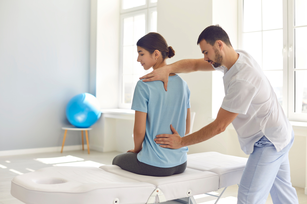 Osteopathic medicine and physiotherapy. Licensed osteopath examining young woman in modern hospital office. Chiropractor helping female patient with scoliosis, low back pain or other spine problems