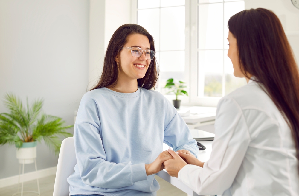 Young female patient rejoices in support of friendly doctor or nurse during medical examination. Professional female doctor tells patient good news by